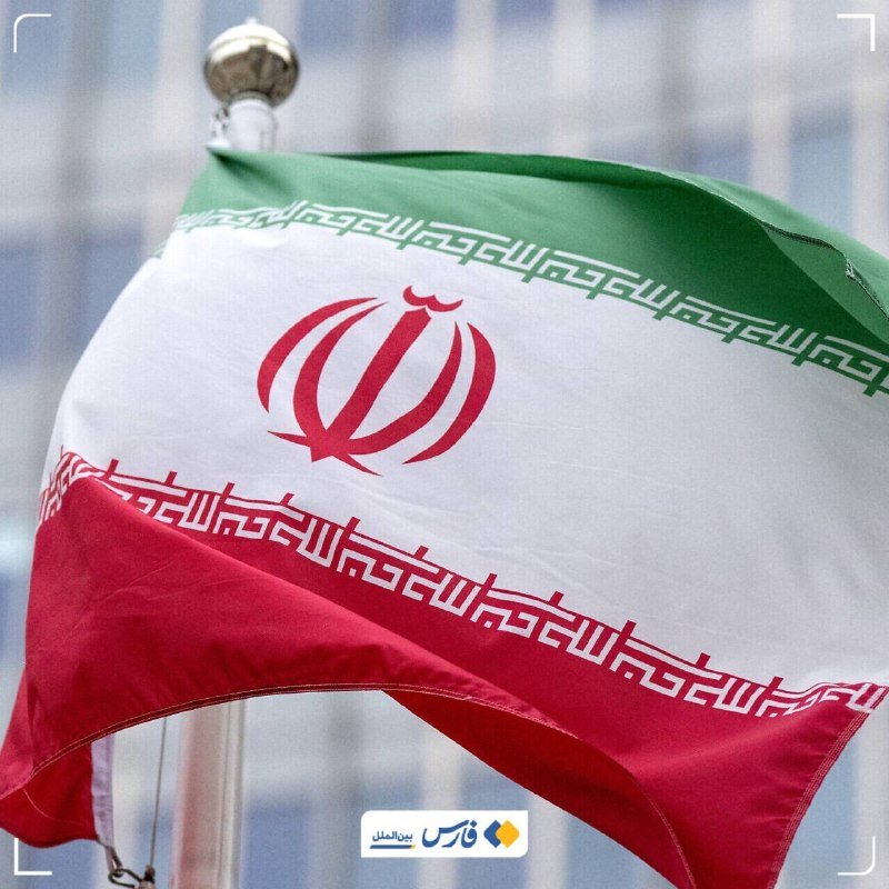The Iranian flag waves against a blurred background, with a logo visible in the bottom corner.