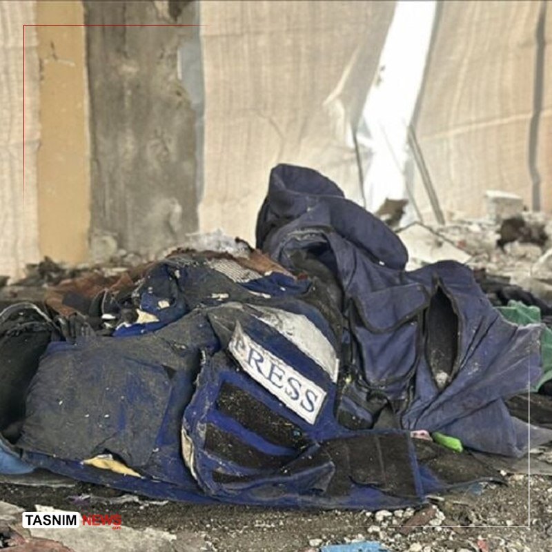 A damaged blue protective vest bearing the letters "PRESS" lies amid rubble and debris in a destroyed structure.
