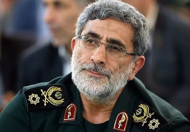 A gray-haired, bearded man wearing glasses and a green military uniform with insignia looks off-camera.