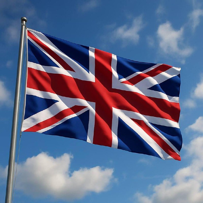 A Union Jack flag waves from a metal flagpole against a partly cloudy blue sky.