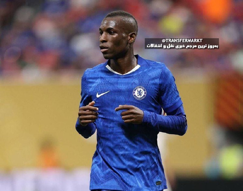A soccer player in a blue jersey with a white crest runs on the field during a match, with a blurred crowd in the background.