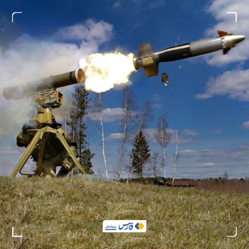 A soldier in camouflage operates a tripod-mounted missile launcher in a grassy field, firing a missile that streaks across the sky amid a plume of flame and smoke.