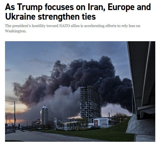 A large plume of dark smoke rises from behind a high-rise building under construction in an urban setting at dusk.