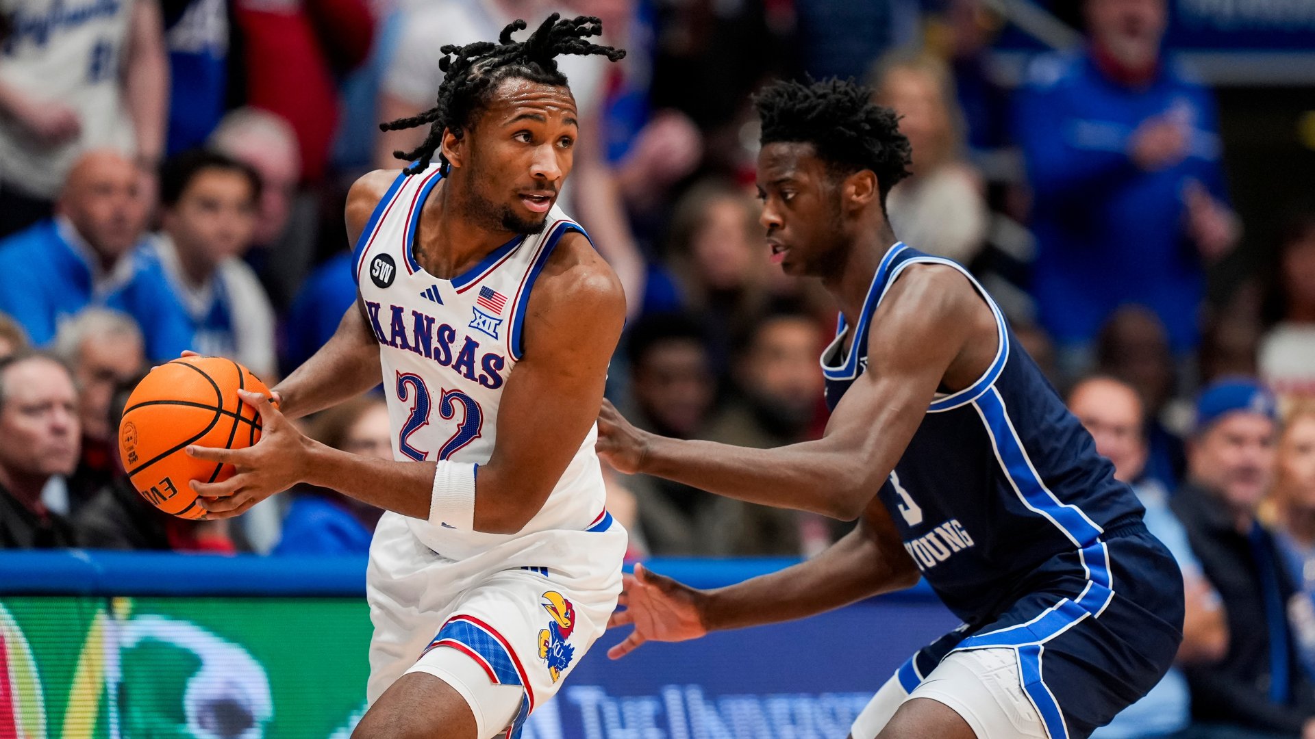 A Kansas basketball player wearing #22 holds the ball while being defended by a BYU player in a blue uniform during a game.