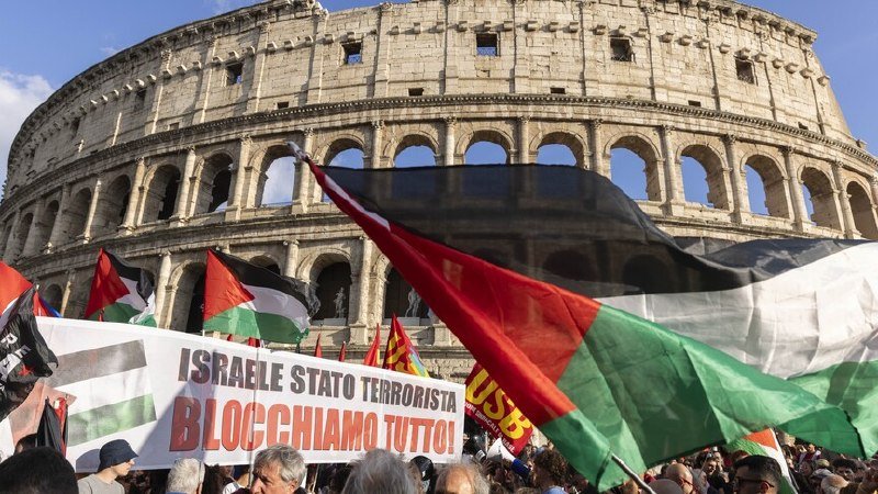 Demonstrators wave Palestinian flags and hold a banner reading "ISRAELE STATO TERRORISTA BLOCCHIAMO TUTTO" in front of the Colosseum in Rome.