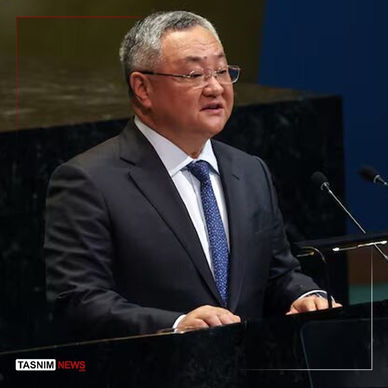 A gray-haired man in a dark suit and glasses speaks at a podium with microphones in a formal setting.