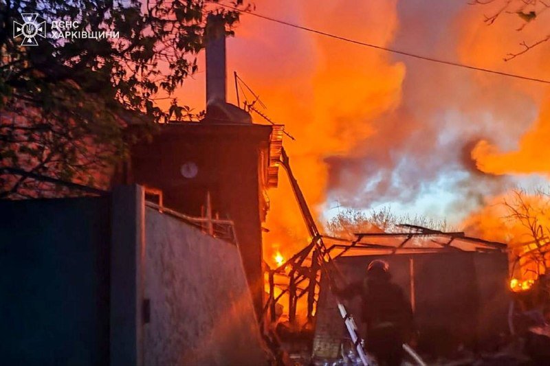 Large flames and thick smoke engulf a building at night, with firefighters on a ladder spraying water onto the blaze, while a logo reading "ДСНС ХАРКІВЩИНИ" appears in the upper left.
