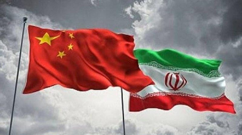 The flags of China and Iran wave side by side on flagpoles against a backdrop of dark, cloudy skies.