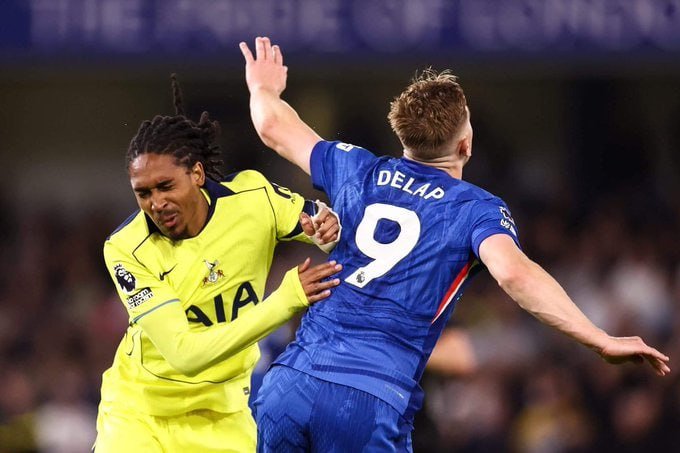 Two soccer players, one in a yellow jersey and another in a blue jersey with "DELAP" and "9" on the back, collide while contesting the ball during a match.