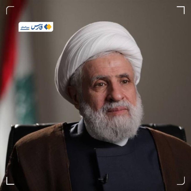 An elderly bearded man wearing a white turban and brown robe sits indoors, with a partially visible flag in the background and a Persian-language news logo overlaid.