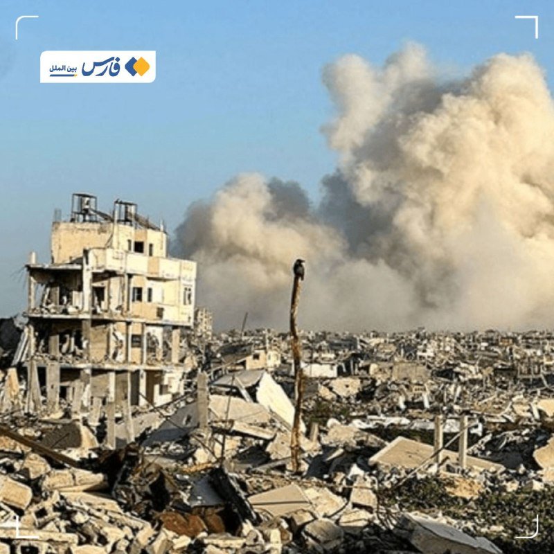 A heavily damaged multi-story building stands amid widespread rubble and debris, with a large plume of smoke rising in the background.