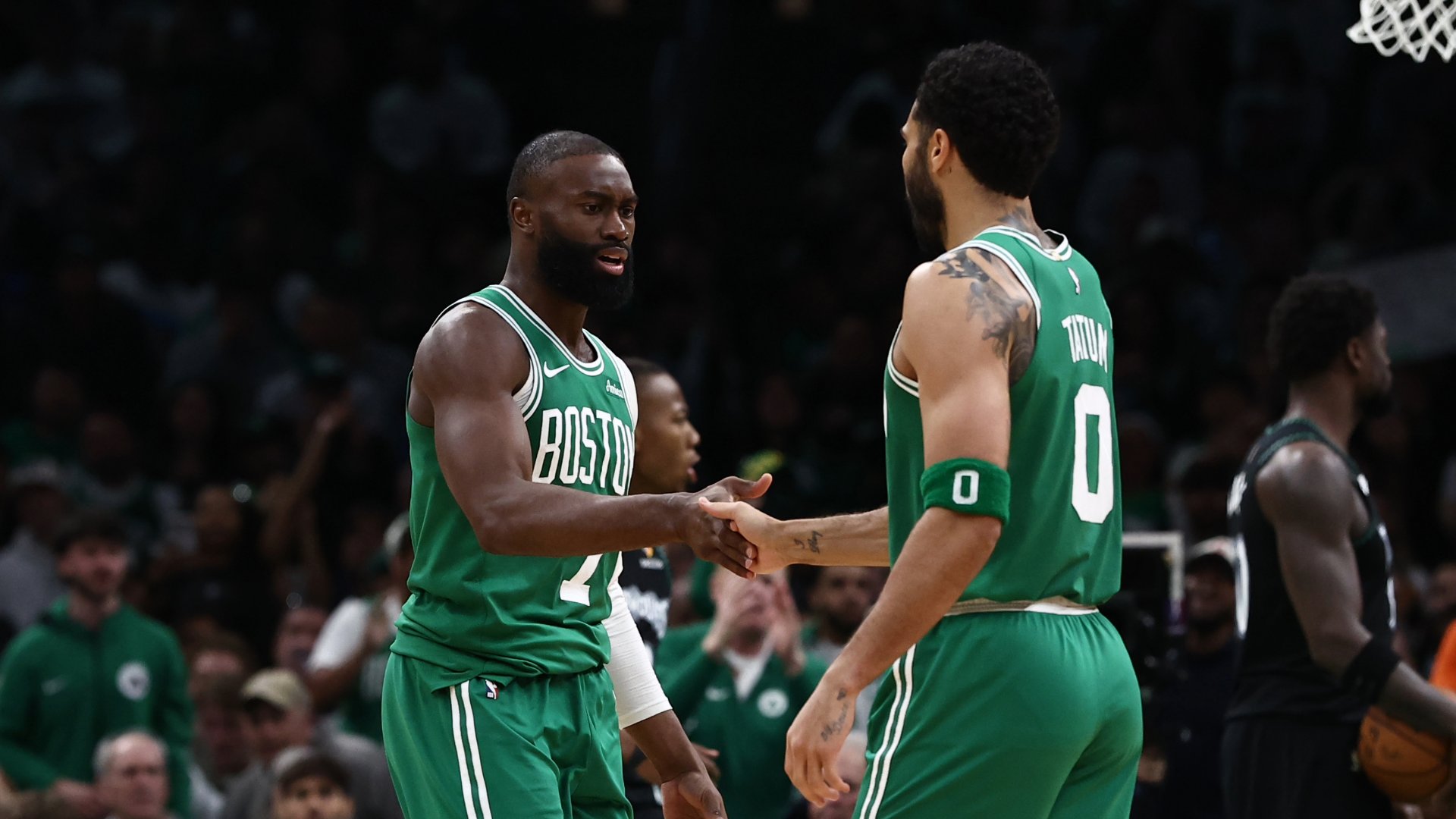 Two Boston Celtics players in green jerseys shake hands on the court during a game against an opposing team in black uniforms.