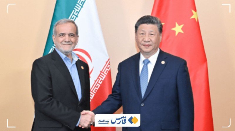 Two men in dark suits shake hands in front of the Iranian and Chinese national flags, with a news outlet's logo visible at the bottom.