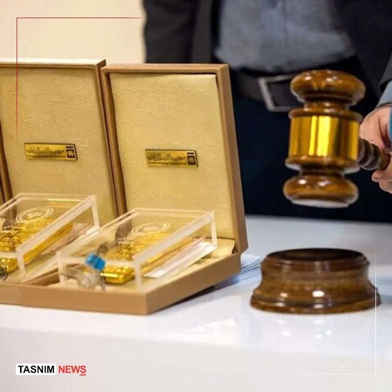 A person in a suit strikes a wooden gavel beside an open display case containing gold items on a white table.