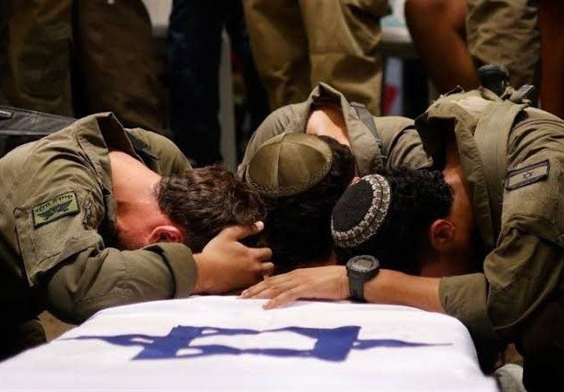 Soldiers in olive-green uniforms kneel and bow their heads over a casket draped with a white cloth bearing a blue Star of David.