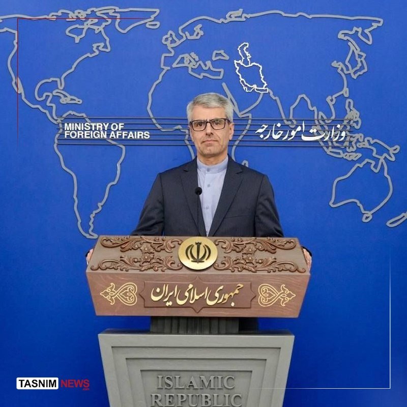 A man in a suit stands at a podium displaying the emblem of the Islamic Republic of Iran, in front of a blue backdrop labeled "Ministry of Foreign Affairs" with a world map outline.
