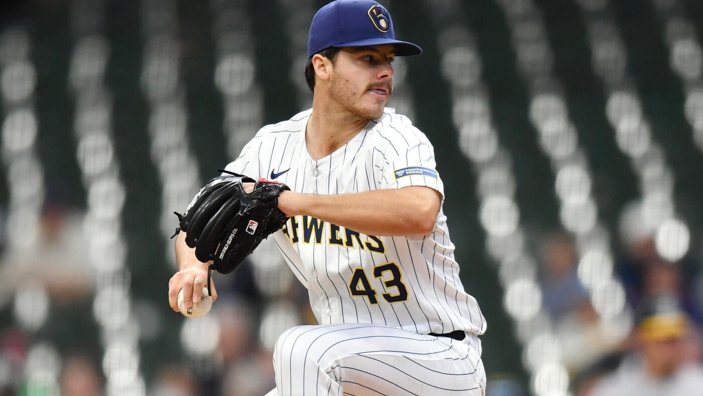 A baseball pitcher wearing a white pinstriped Brewers jersey with the number 43 winds up to throw, with a softly blurred stadium background behind him.