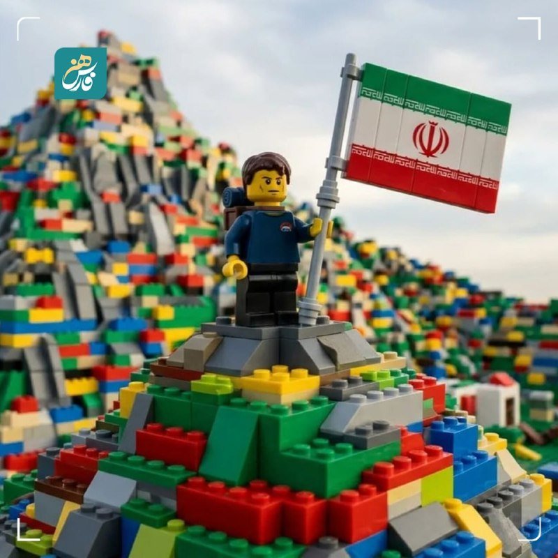 A LEGO figurine holding an Iranian flag stands atop a colorful pyramid of stacked LEGO bricks, with a small logo in the upper left corner.