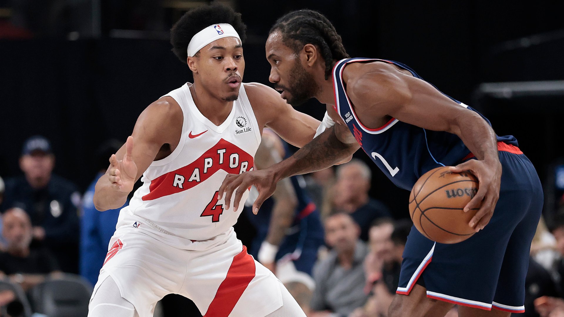 A basketball player in a white Toronto Raptors jersey, number 4, defends against an opponent in a dark blue jersey, number 2, who holds the ball during a game.