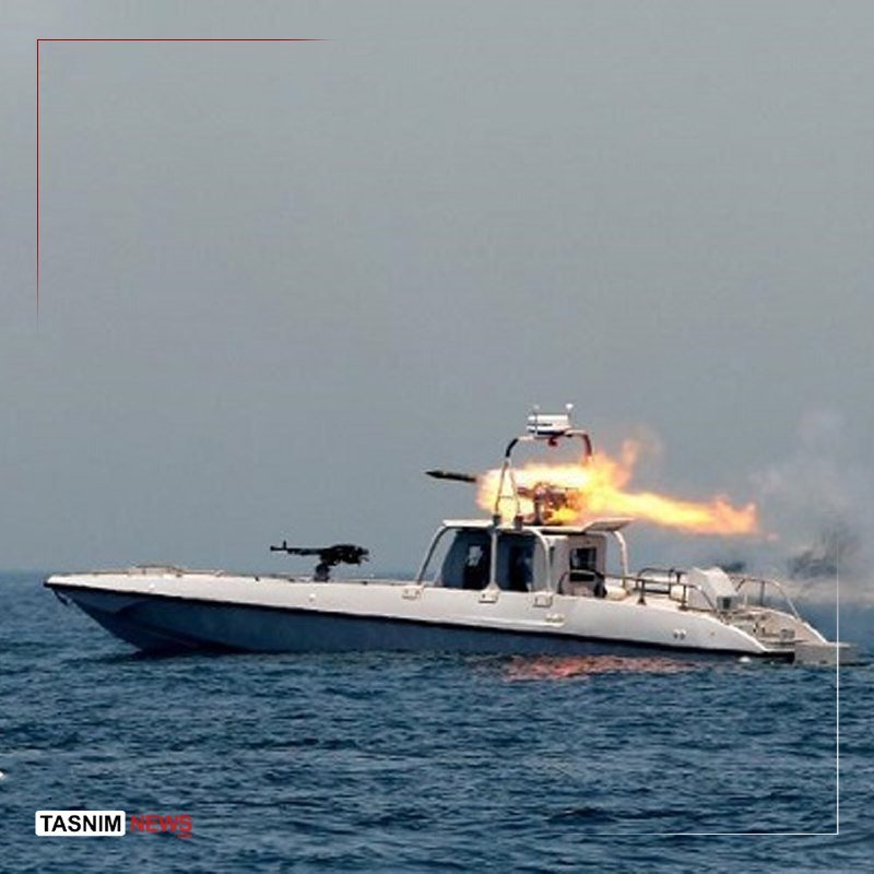 A military patrol boat on open water fires a mounted weapon, with a large flame erupting from its discharge.