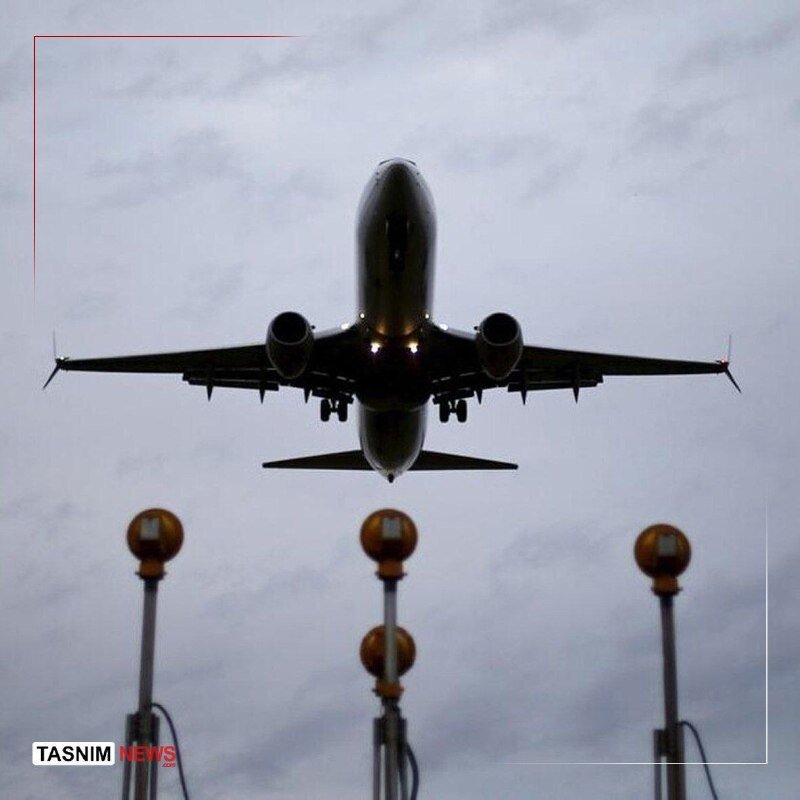 A twin-engine commercial jet takes off against a gray sky, with runway approach lights visible below; the image bears a "TASNIM NEWS" watermark.