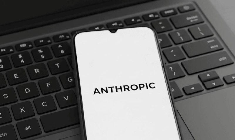 A smartphone displays the "ANTHROPIC" logo on a white screen, resting on a dark laptop keyboard.