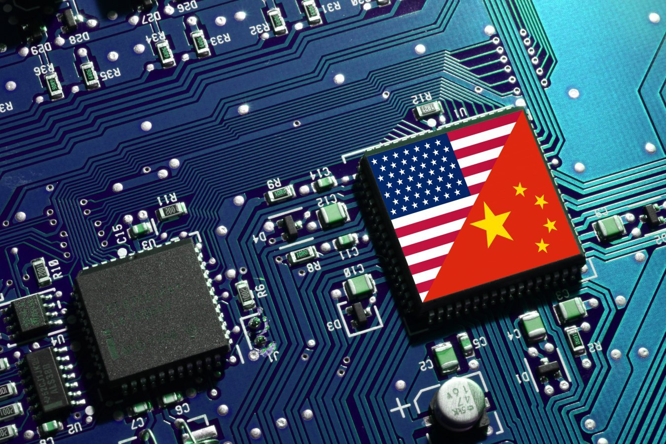 A computer chip displaying the U.S. and Chinese flags rests on a blue circuit board alongside microchips, capacitors, and labeled electronic components.
