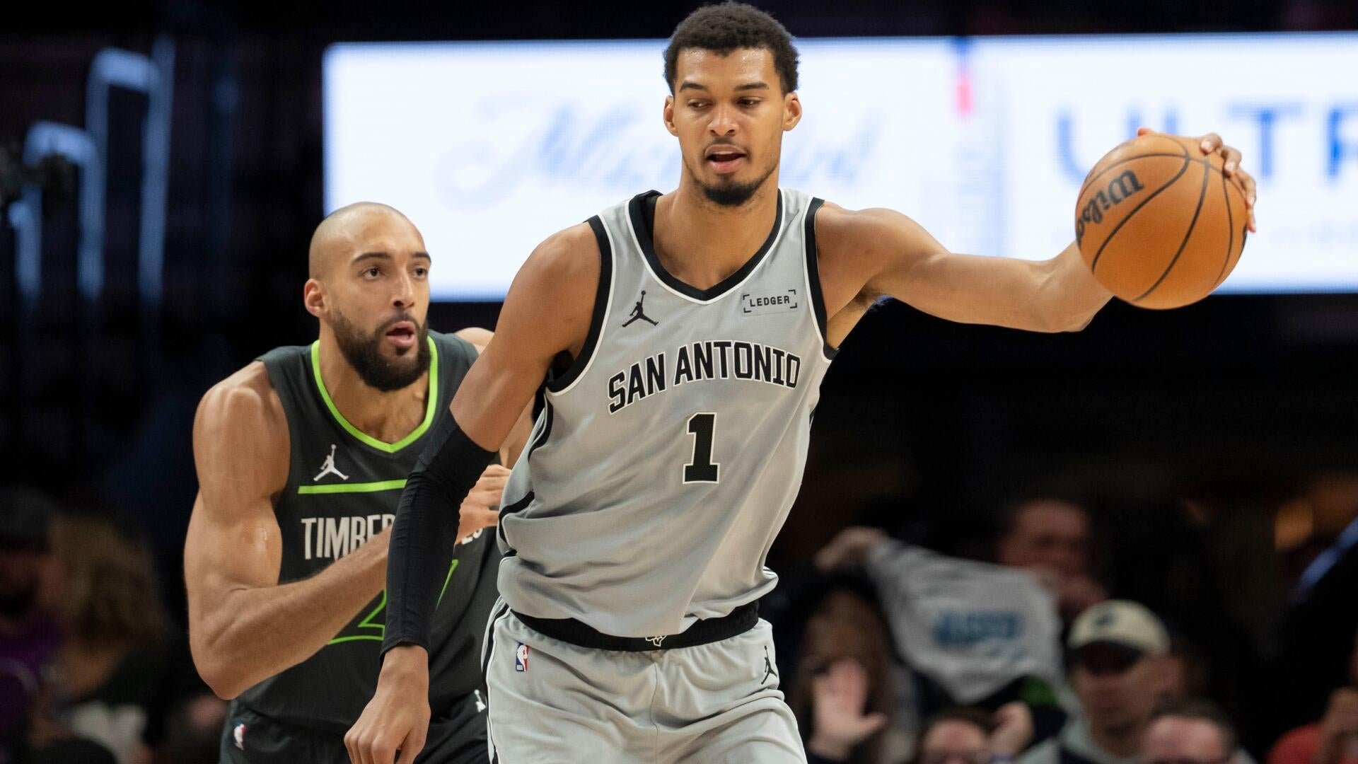 A San Antonio Spurs player wearing jersey number 1 holds a basketball while being defended by a Minnesota Timberwolves player during an NBA game.