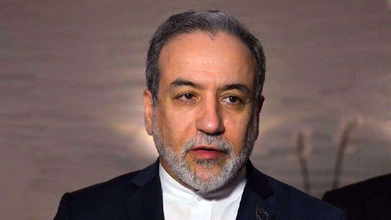 A gray-haired, bearded man in a dark suit and white shirt looks forward against a blurred background.