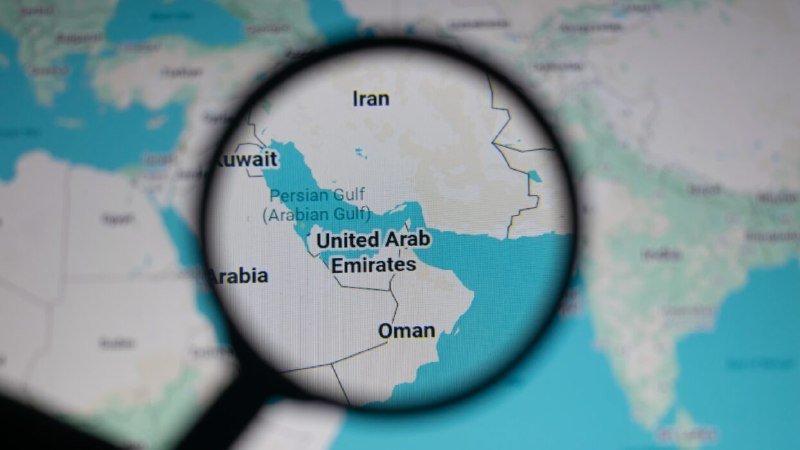 A magnifying glass enlarges a digital map showing Iran, Kuwait, Saudi Arabia, the United Arab Emirates, Oman, and the Persian Gulf region.