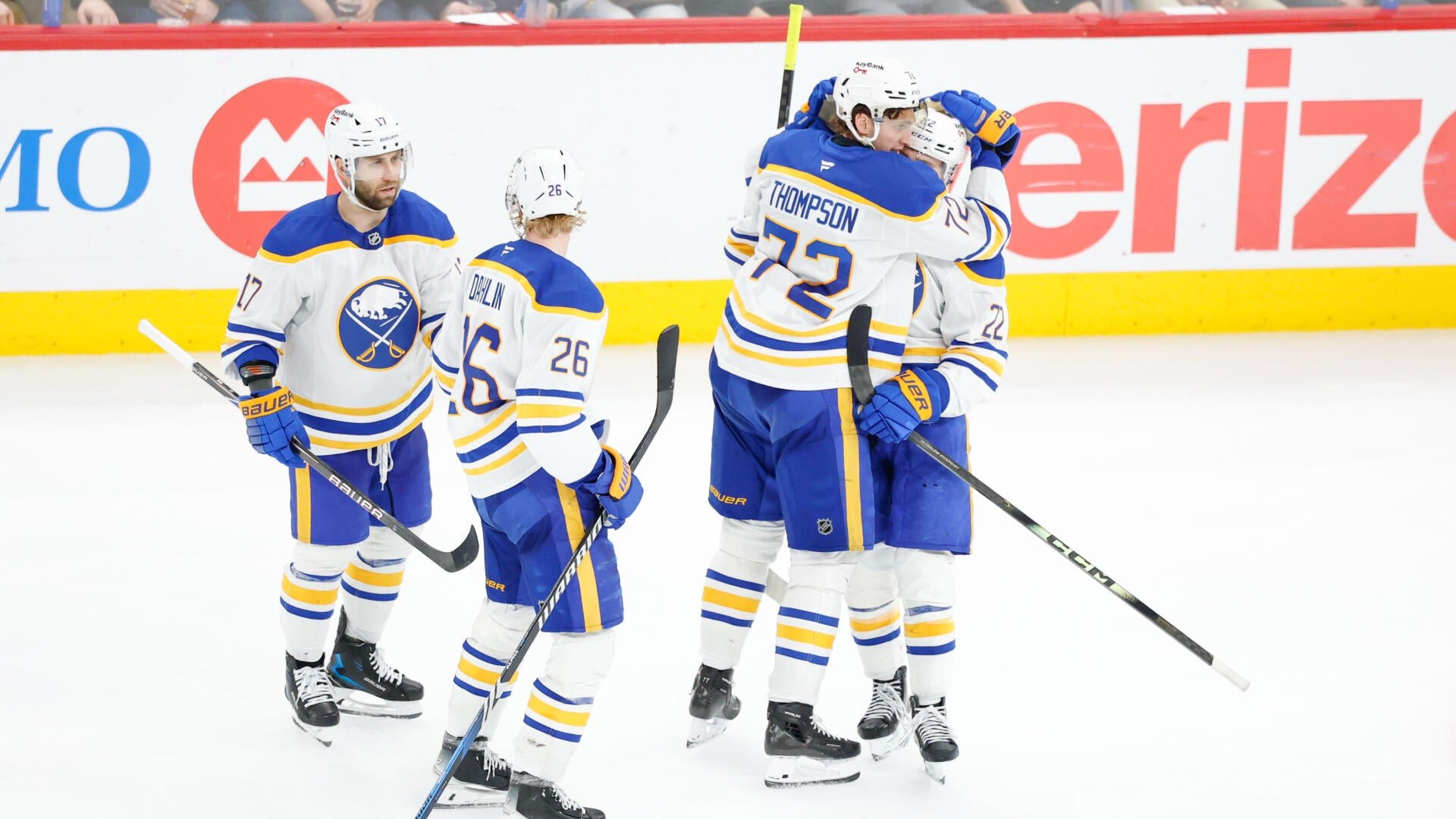 Buffalo Sabres hockey players in white and blue jerseys celebrate on the ice, with two players embracing while teammates, including one wearing number 17 and another labeled "Dahlin 26," skate nearby.