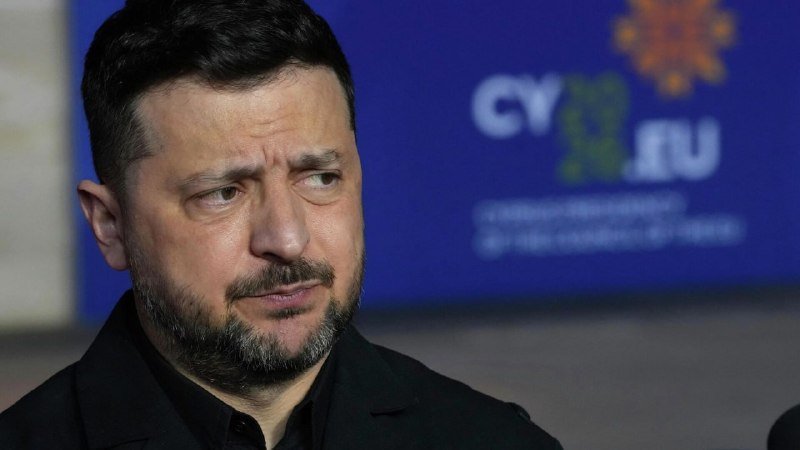 A bearded man in a dark jacket looks to the side during an event, with a blurred blue backdrop featuring "СУПЕР" text and a star-shaped logo behind him.