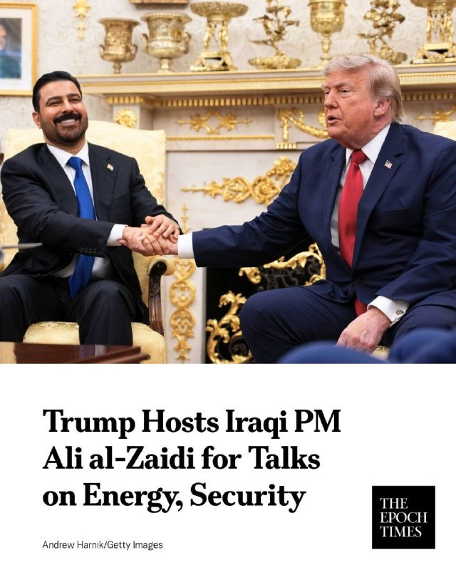 Two men in dark suits shake hands while seated in an ornately decorated room featuring gold-toned decorative vases on a mantelpiece behind them.