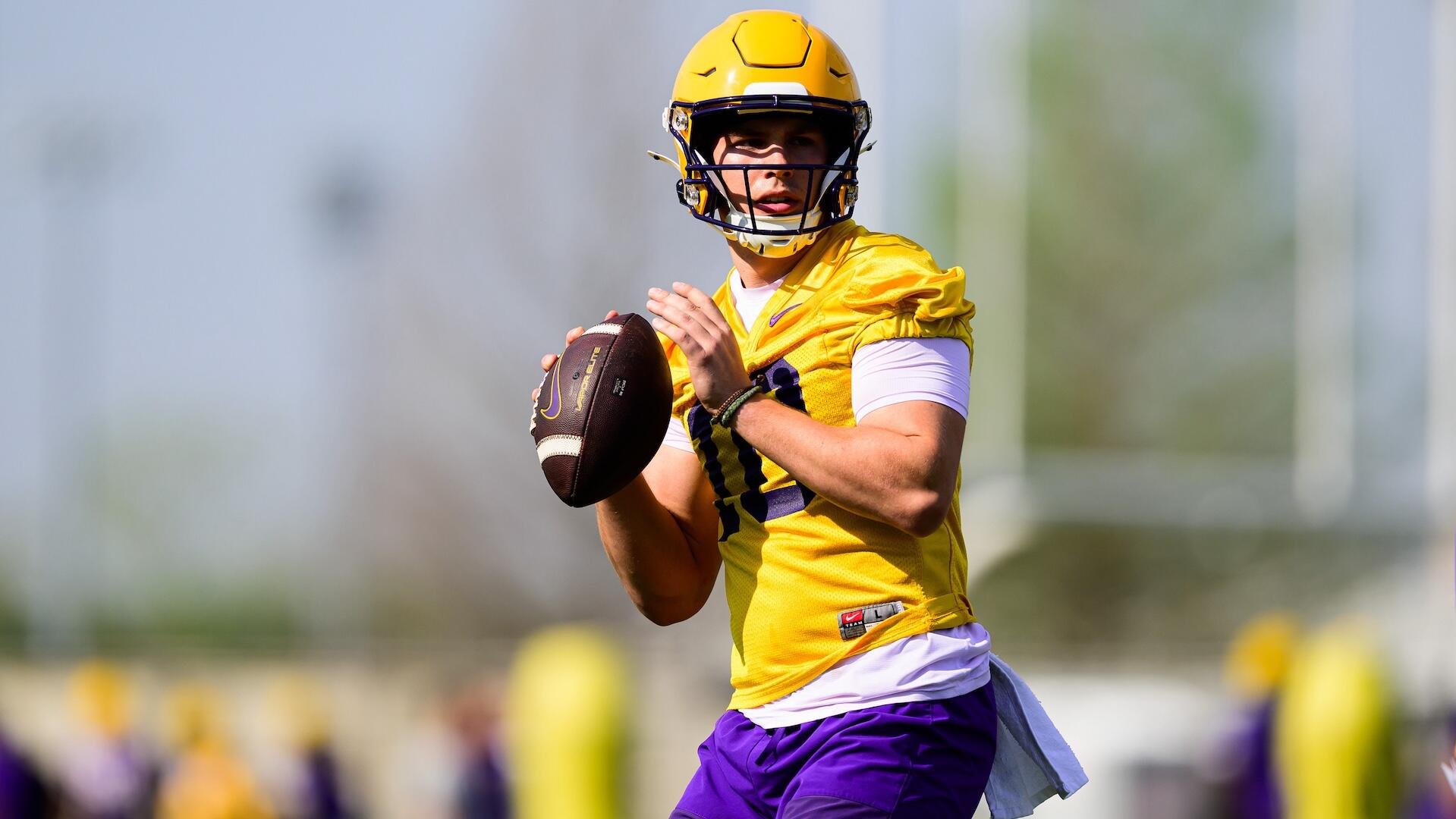 A football player in a yellow jersey and helmet prepares to throw a football during an outdoor practice.