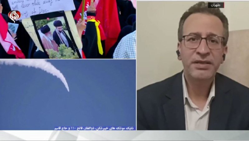 A split-screen news broadcast shows protesters holding flags and a framed portrait on the left, alongside footage of a smoke trail in the sky, while a man with glasses appears on the right.