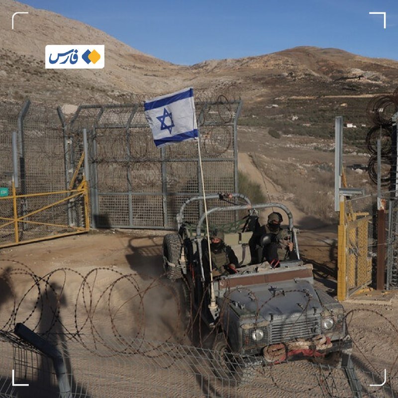 An Israeli flag flies from a military vehicle carrying soldiers as it drives through a barbed-wire gate in a hilly, arid landscape.