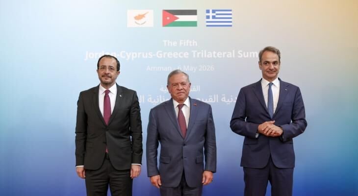 Three men in suits stand posed before a backdrop displaying three national flags and text reading "The Fifth Jordan-Cyprus-Greece Trilateral Summit, Amman, 11 May 2026."