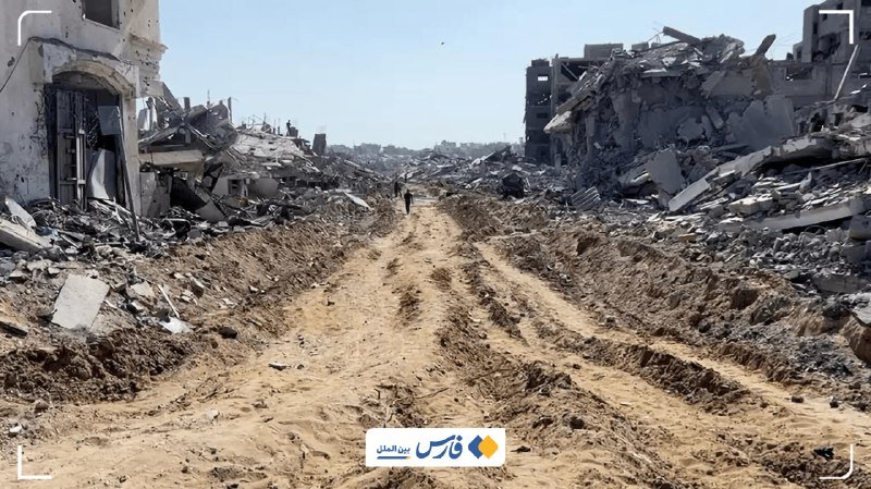 A person walks down a dirt road flanked by extensive rubble and destroyed buildings under a clear sky, with Arabic text overlaid at the bottom.