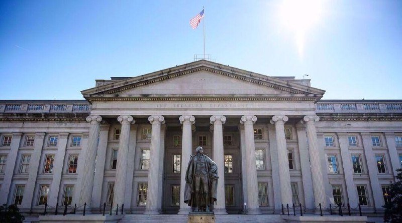 A neoclassical stone building with large columns and the inscription "THE TREASURY DEPARTMENT" features a bronze statue in front and an American flag atop.