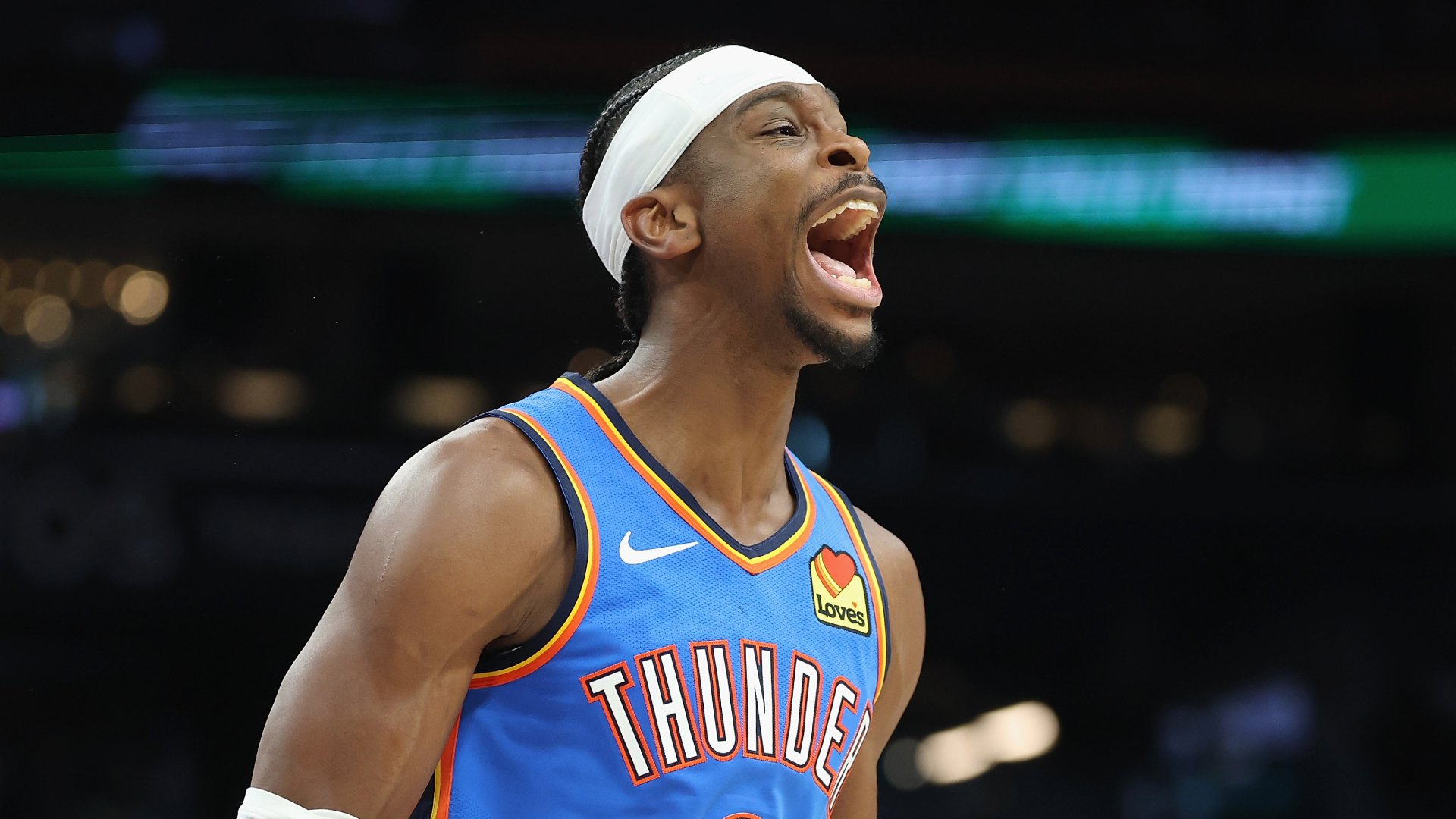 A basketball player in a blue Thunder jersey and white headband yells with his mouth wide open during a game.