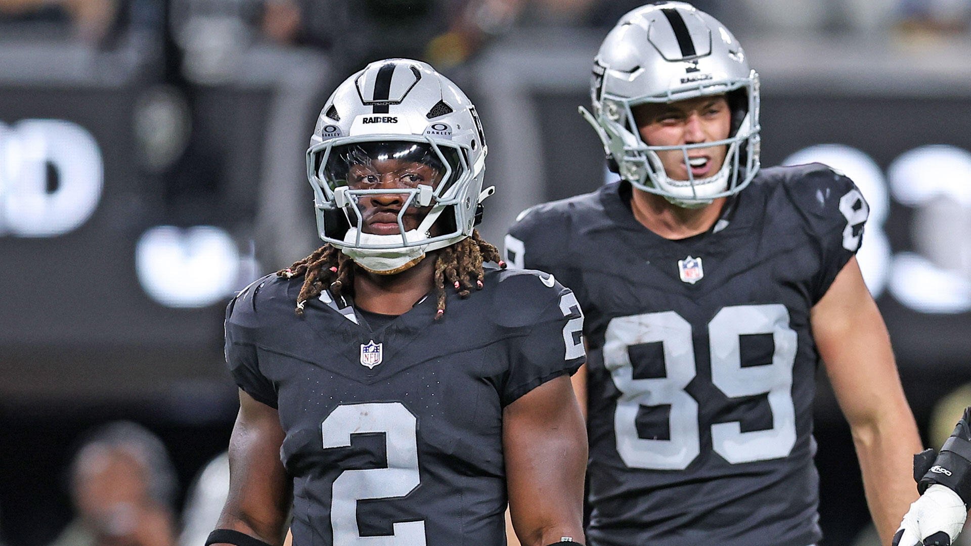 Two Las Vegas Raiders football players in black jerseys and silver helmets stand on the field, one wearing number 2 and the other number 89.