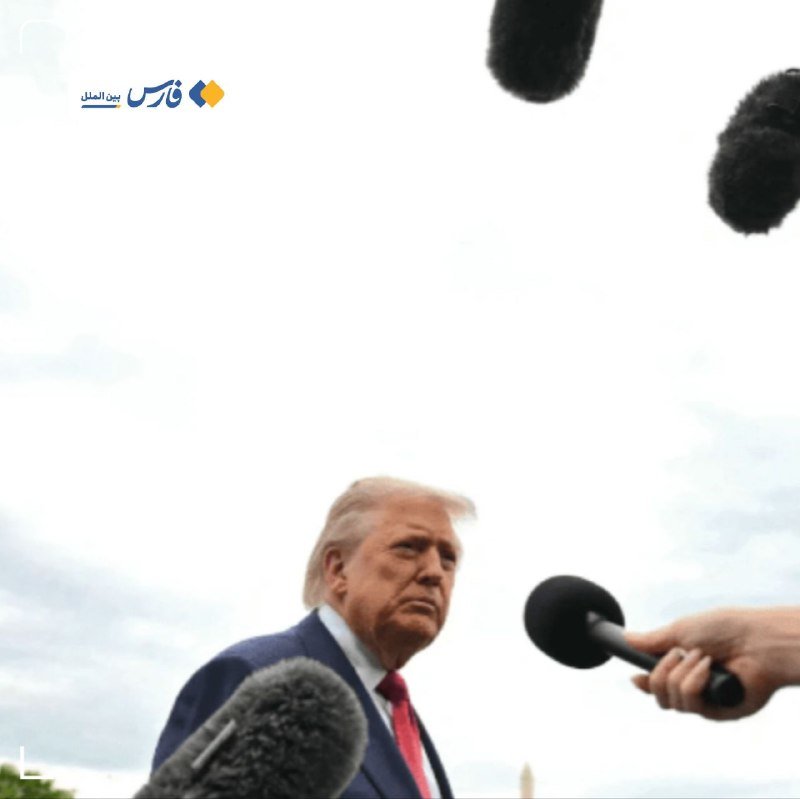 A man with blonde hair in a blue suit and red tie speaks to reporters outdoors, surrounded by multiple microphones held up to him.