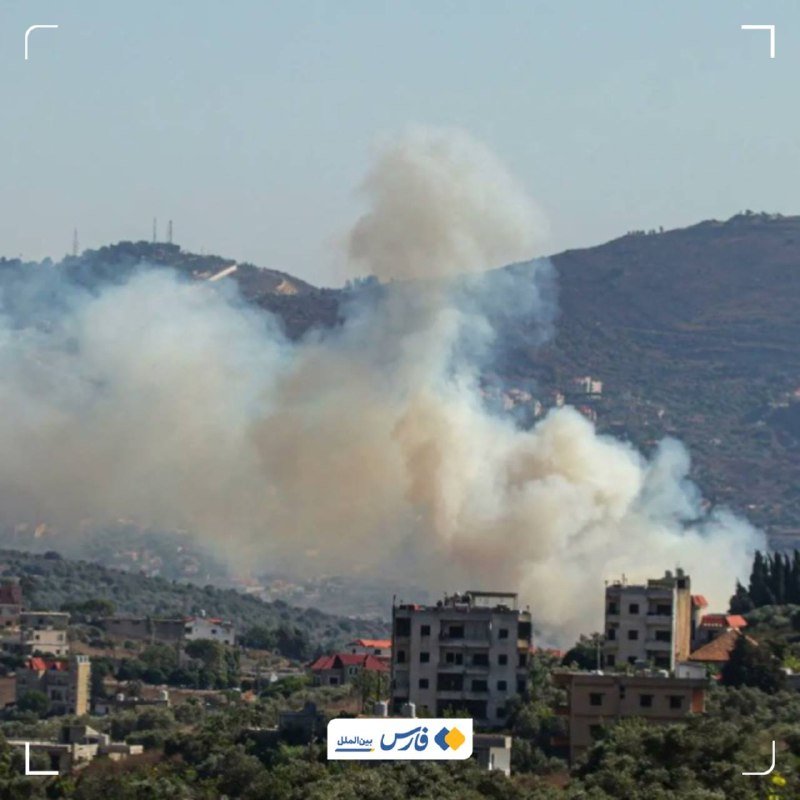 Large plumes of gray and white smoke rise above a hillside town with buildings and trees under a clear sky.