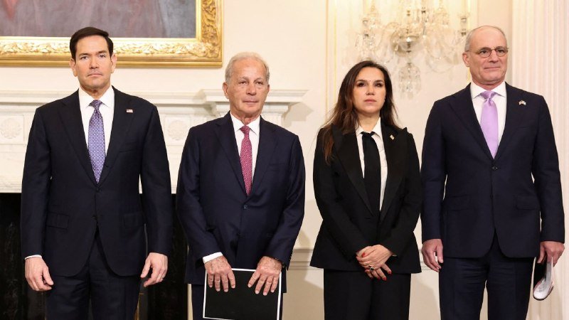 Four people in formal business attire stand side by side in an ornate room featuring a chandelier and a gold-framed painting.