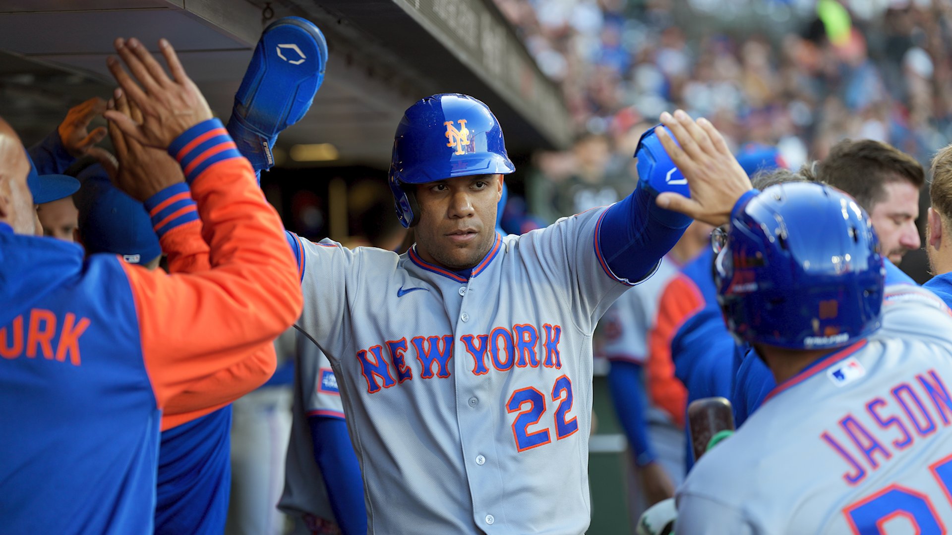 A New York Mets player wearing jersey number 22 exchanges high-fives with teammates in the dugout after scoring.