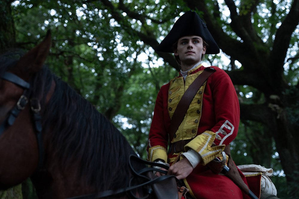 A man in a red and gold 18th-century military uniform and black tricorn hat sits on a dark horse beneath a large tree, gazing upward.