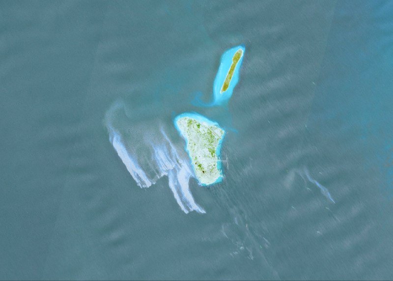 An aerial view shows two small islands with white sandy beaches and green vegetation, surrounded by turquoise water with visible sediment plumes.