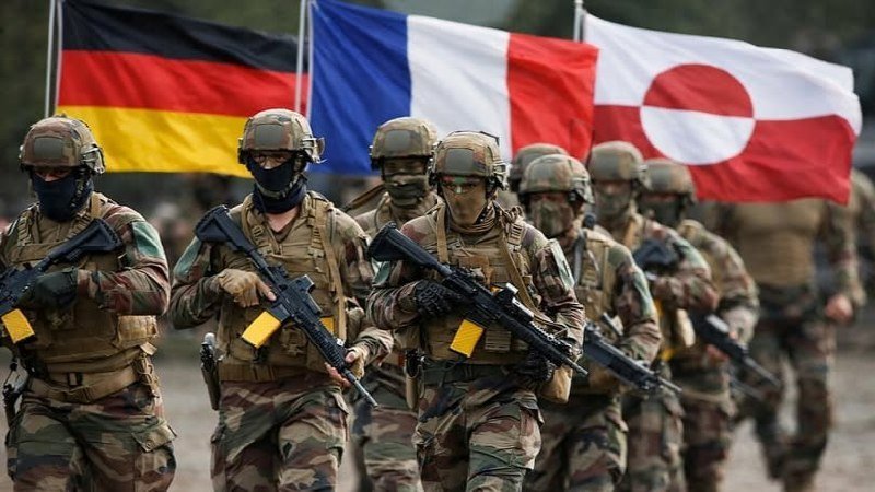Soldiers in camouflage uniforms and helmets march forward carrying rifles, with German, French, and Greenlandic flags displayed behind them.