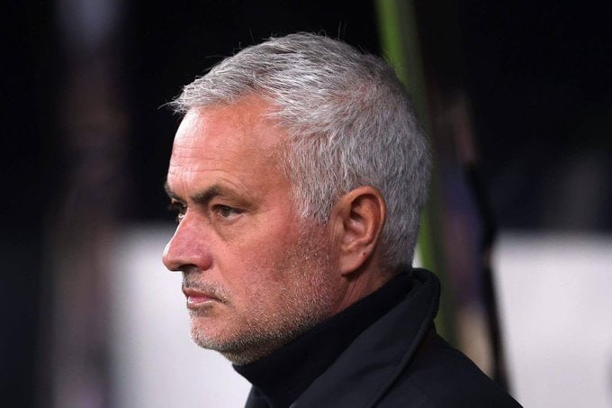 A gray-haired man in a black coat looks to the side in profile against a dark background.