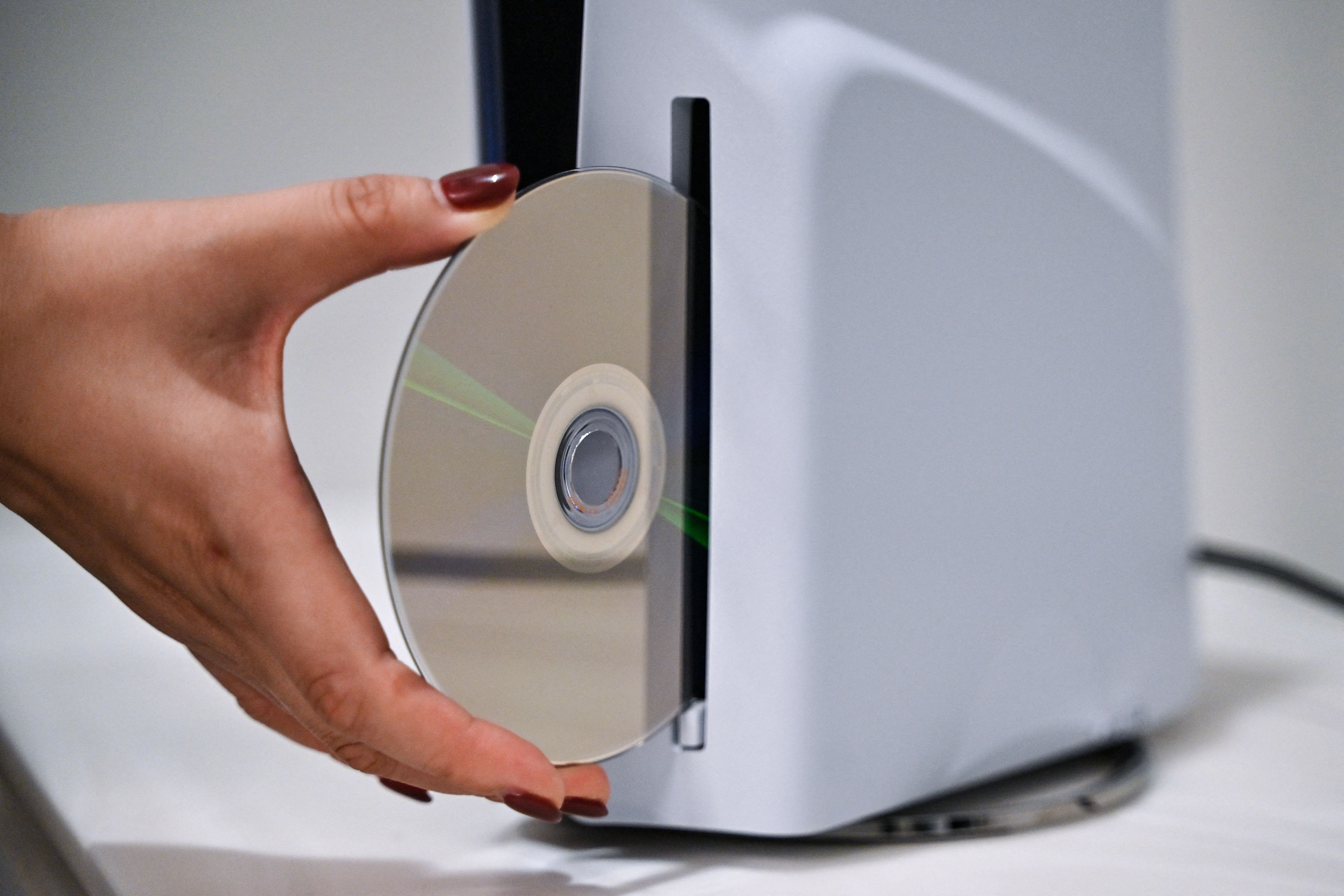 A hand holds a reflective disc against the slot of a white, square electronic console.